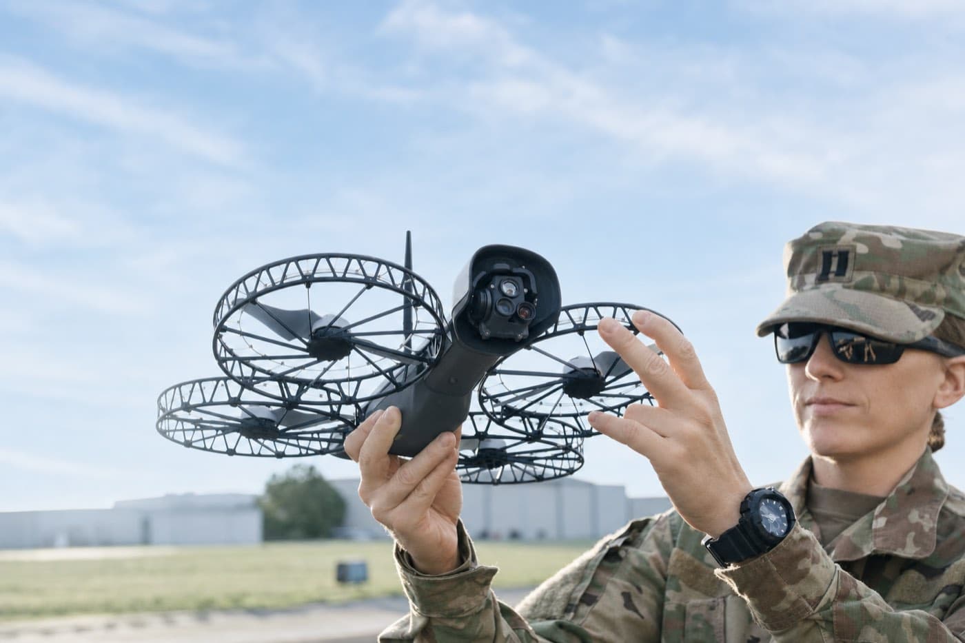 An operator in uniform holding a caged quadcopter, checking it before flight